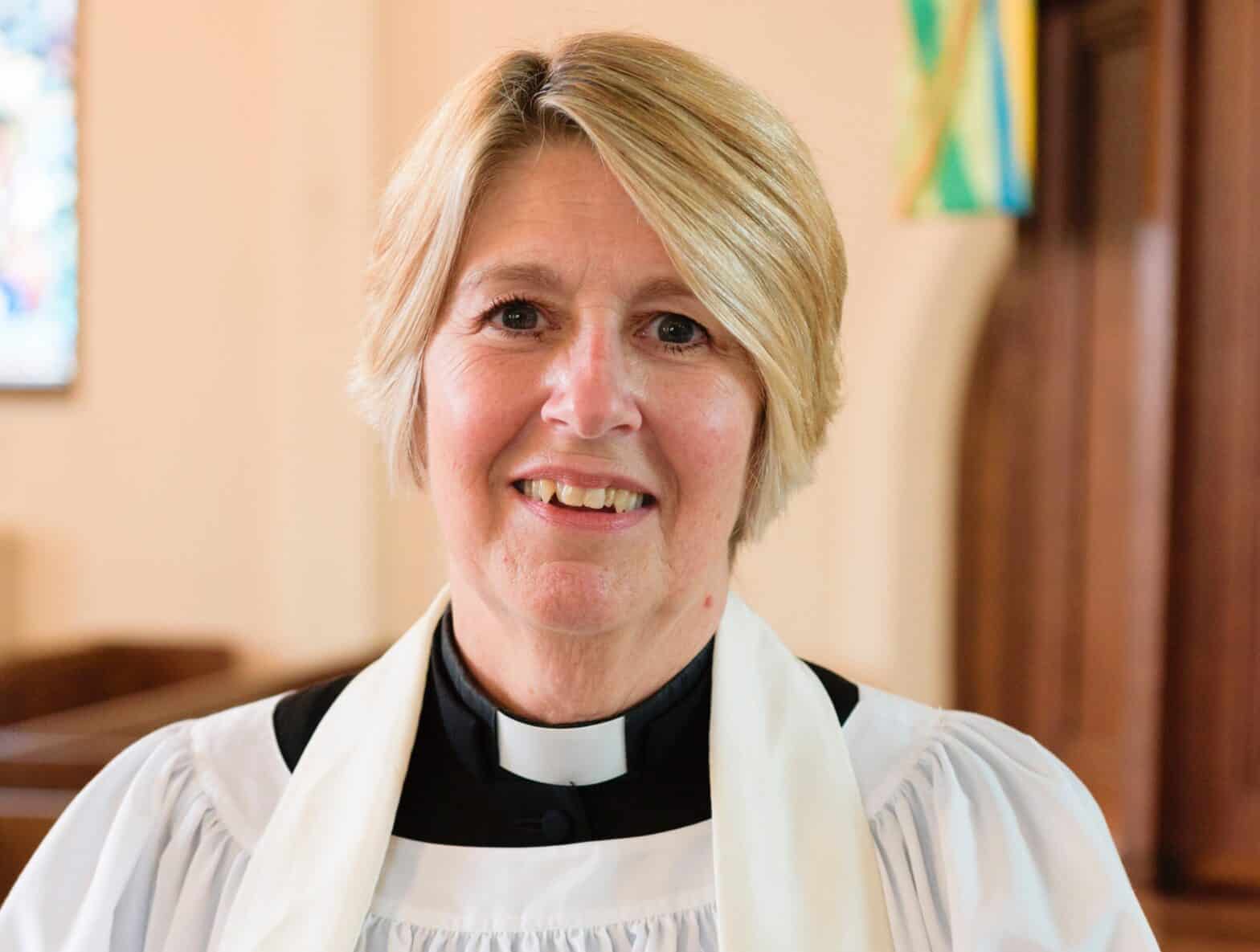 A female vicar smiling into the camera.