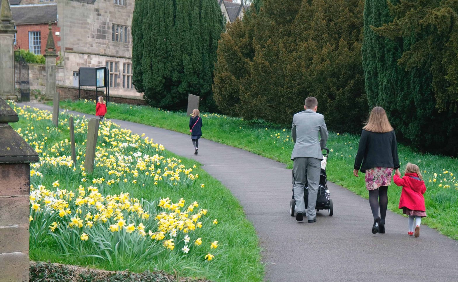 A young family with buggy walking away from the camera up a path towards a church.