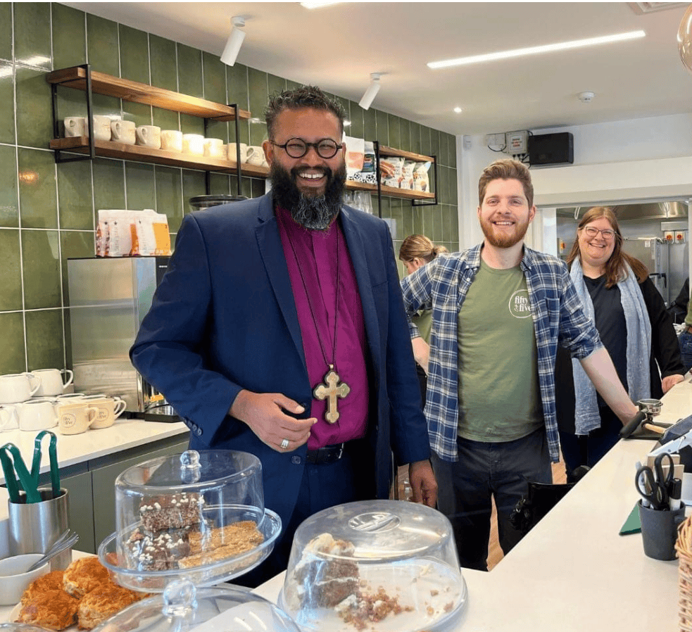 Three people in a cafe, including a bishop helping to serve food