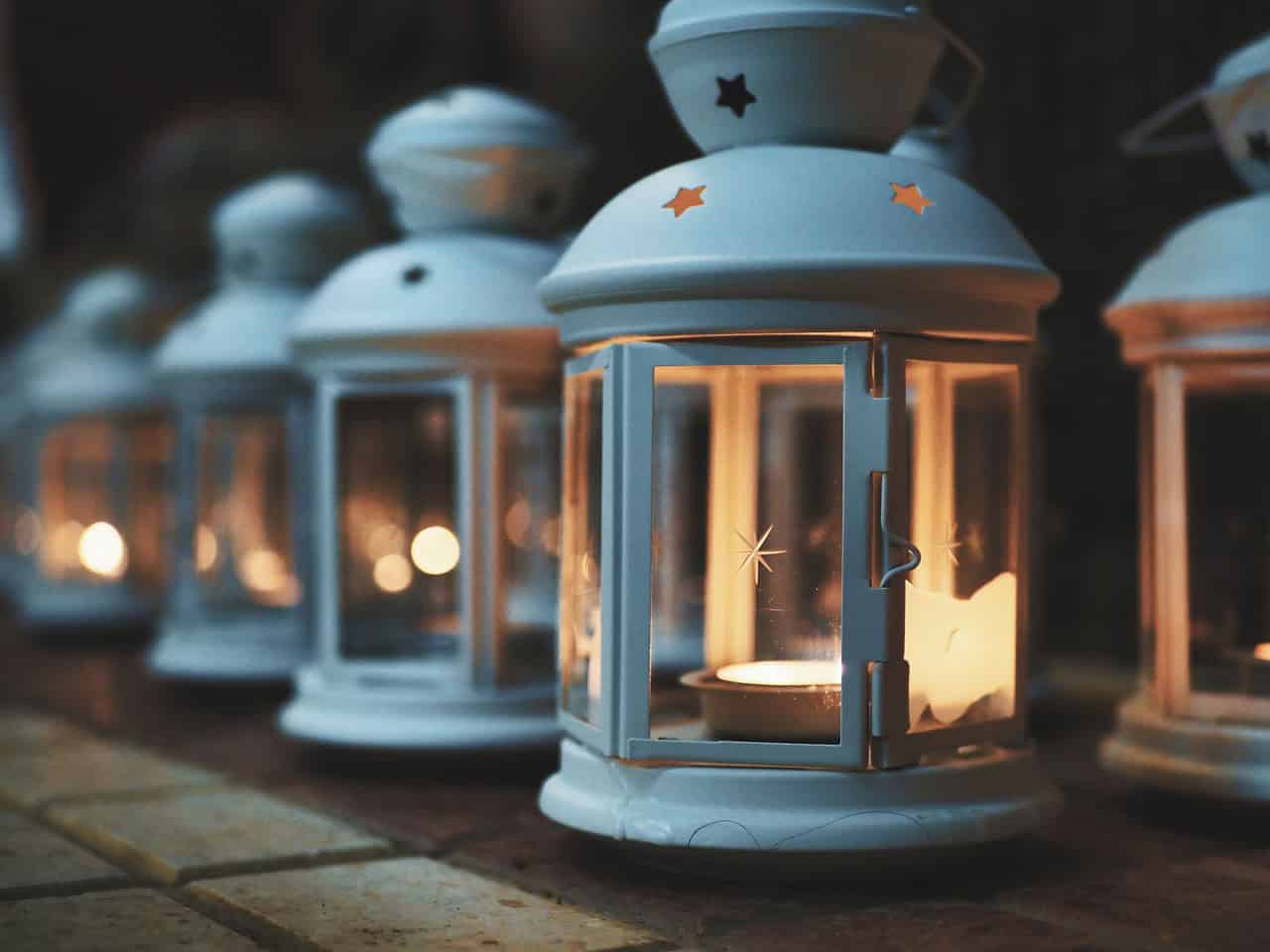A row of white lanterns standing in the dark, each with a lit candle inside.