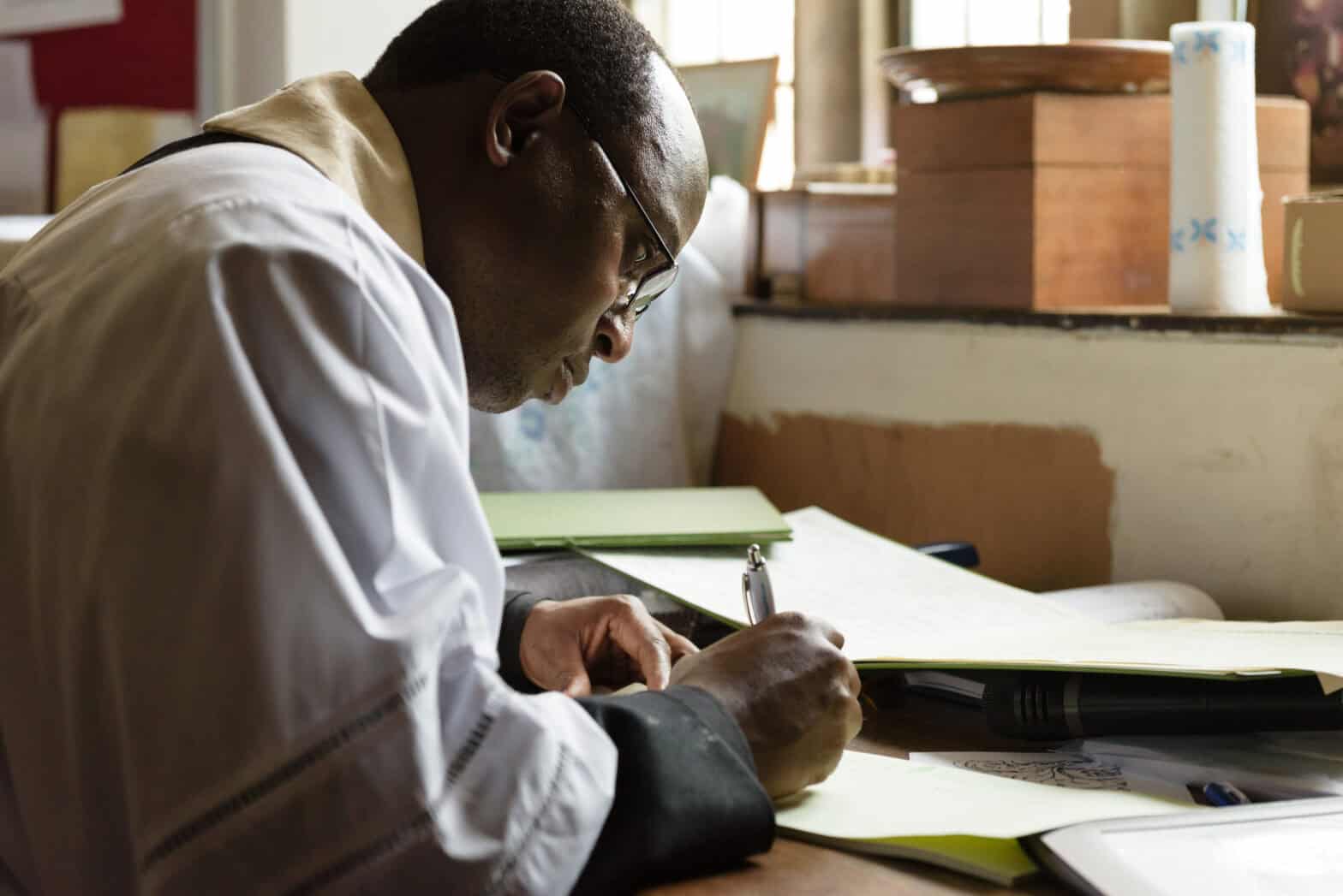 A vicar at a desk busy writing something.