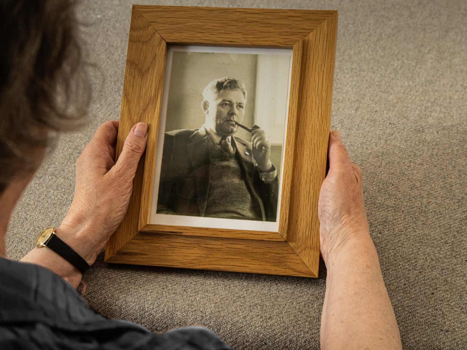 Close up of hands holding a framed black and white photo of a gentleman smoking a pipe.