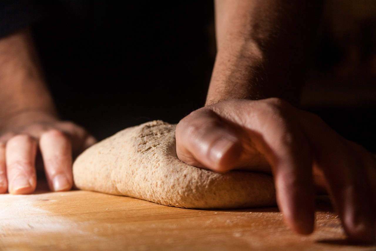 Close up of hands kneading dough on a wooden board.