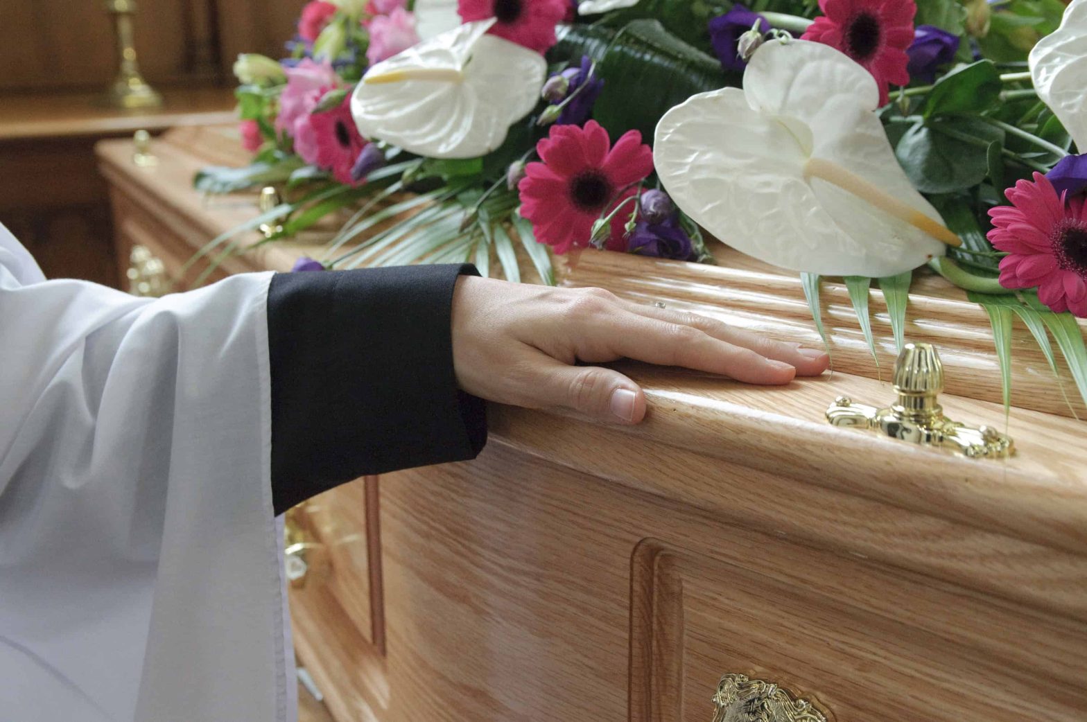 Close up of Ministers hand on a Coffin with pink and white flowers on top.