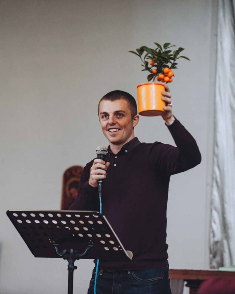 Danny Driver ( a young man with short cropped hair) hiding a plant with small oranges on.