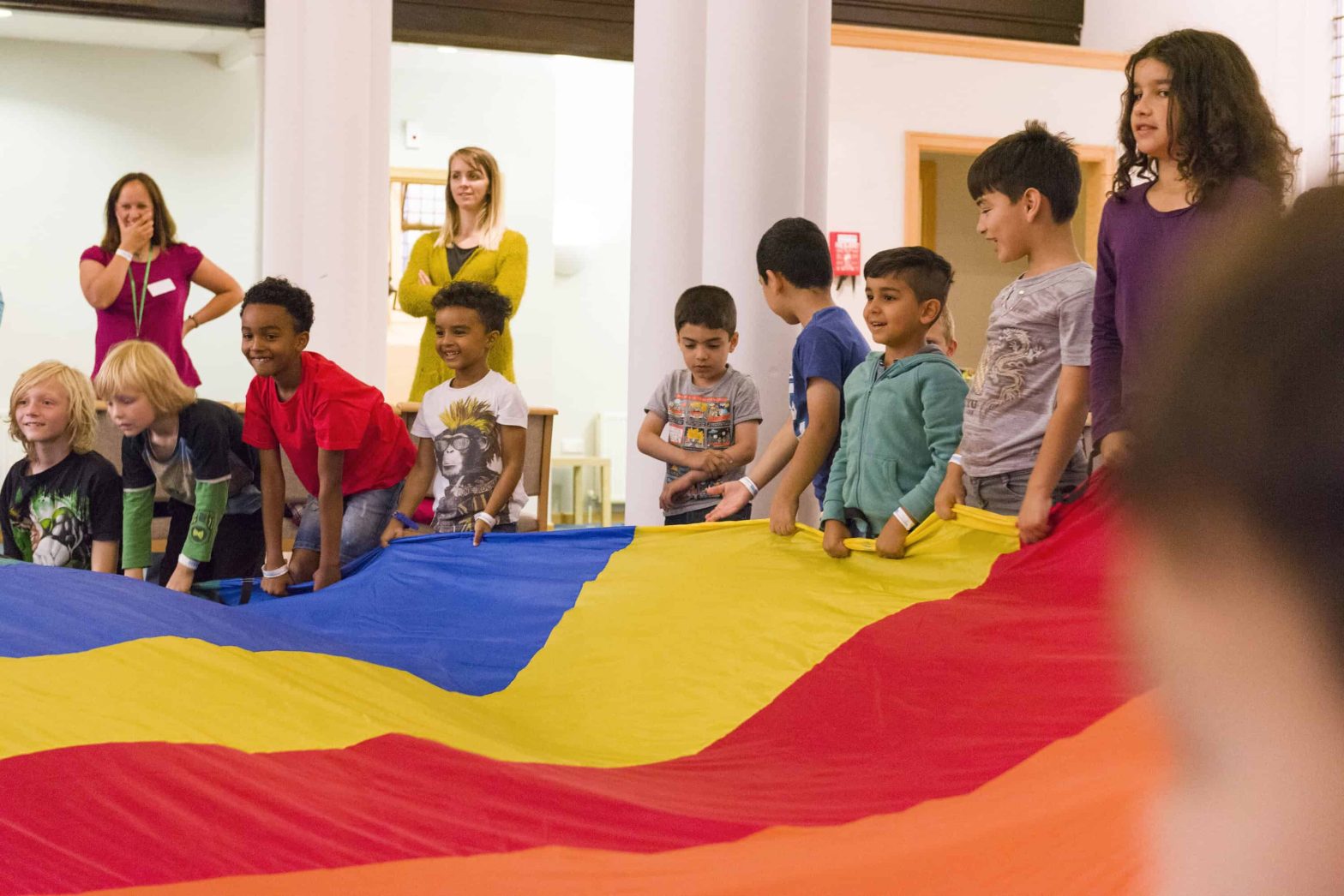 Diverse group of children aged 7 or 8 holding out a rainbow coloured parachute.