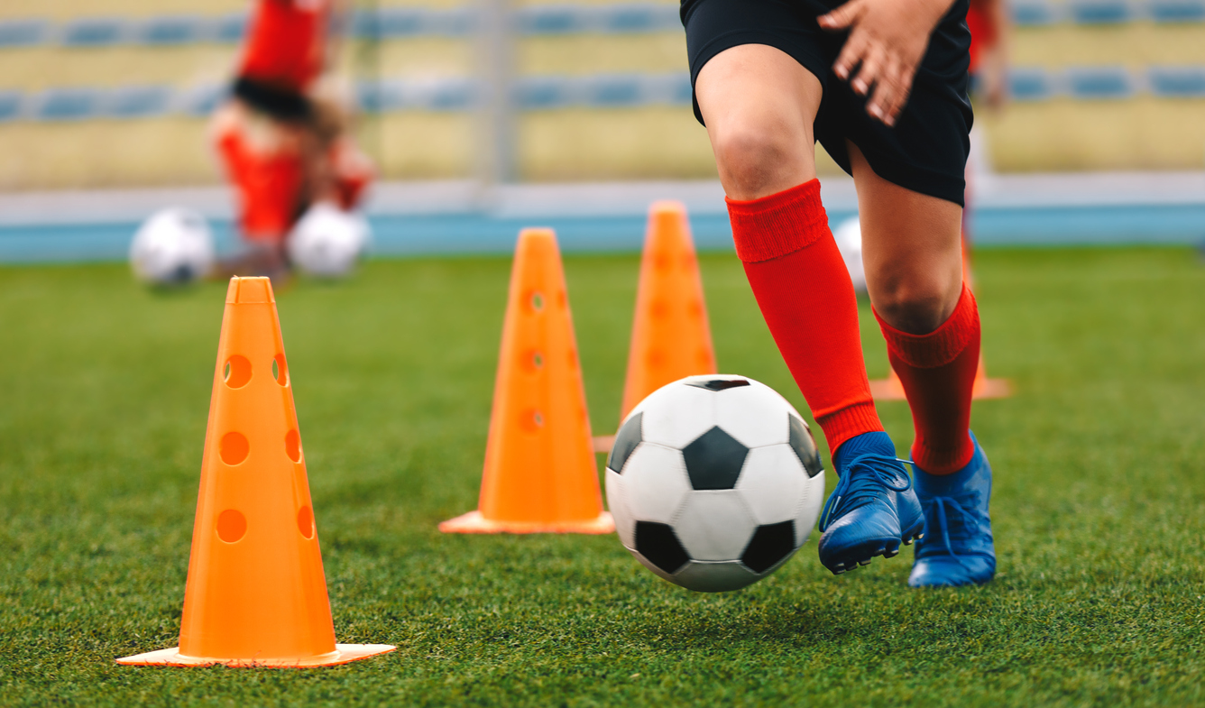 A child dribbling ball in training between orange cones.