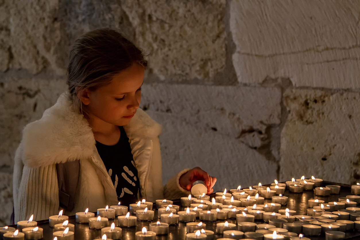 Girl lighting a candle amongst a sea of candles in a church