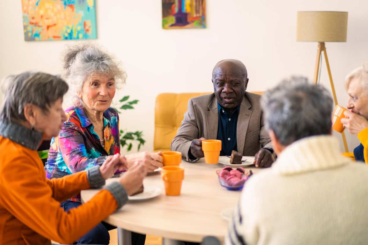 Group of older women and men sat around a table drinking tea and eating cake.