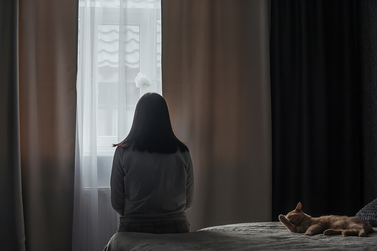 Lone woman silhouetted against a window she is looking out of.