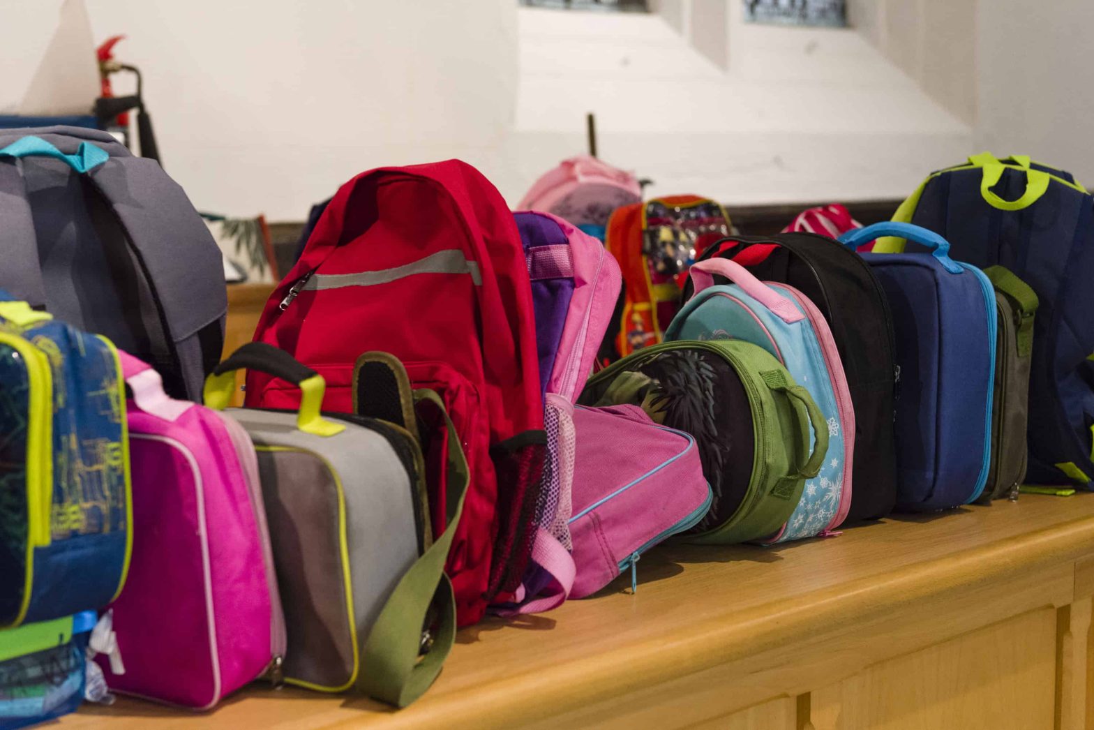 Lots of colourful school bags lined up on a table.