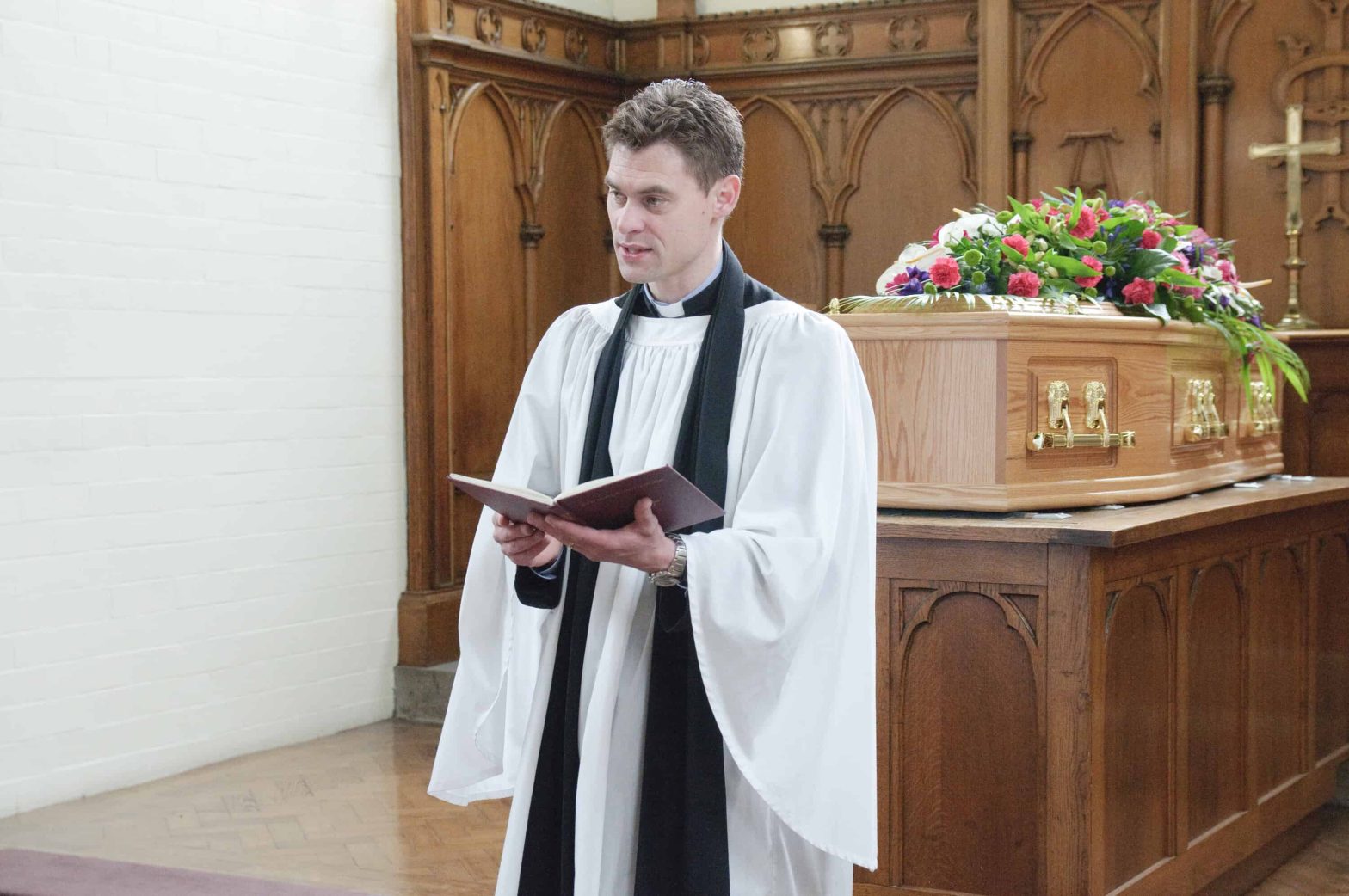 Male vicar stood in front of a coffin in a crematorium leading a funeral.