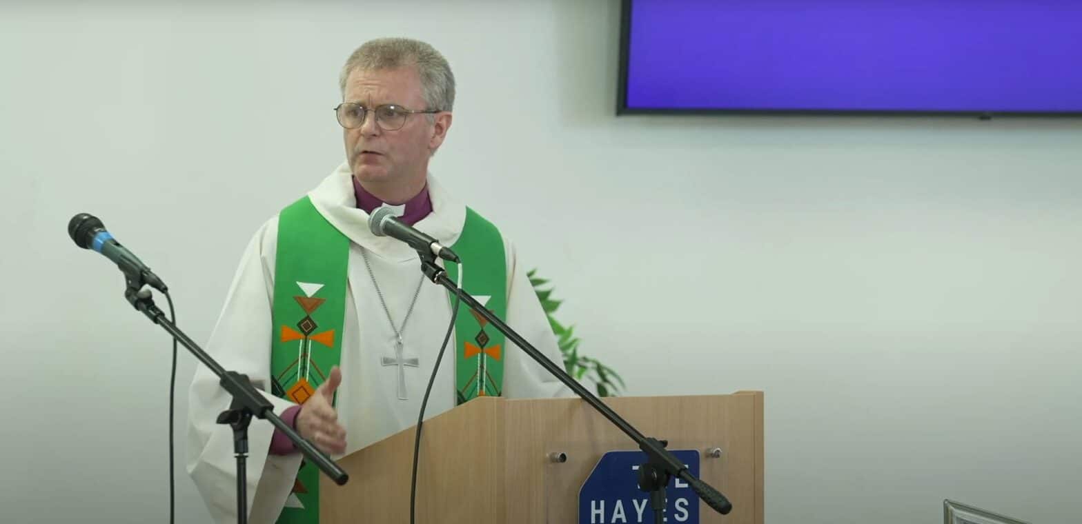 Bishop John Tanner speaking at The Hayes conference centre. Over his purple bishop's shirt hear was a white cassock, green stole with a geometric patten which includes a cross, and a large silver cross on a chain.