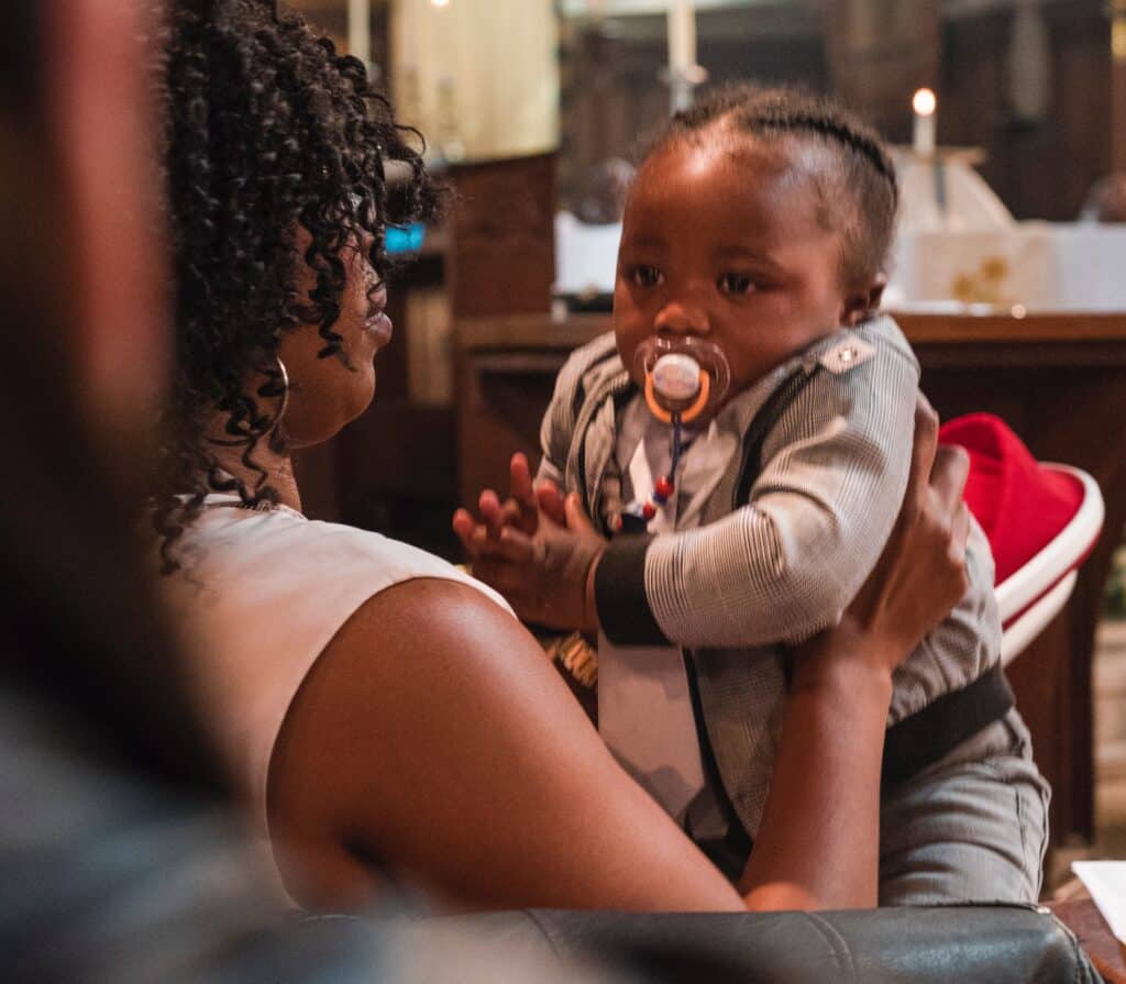 Toddler girl with dummy in mouth being bounced on mums knee in church.