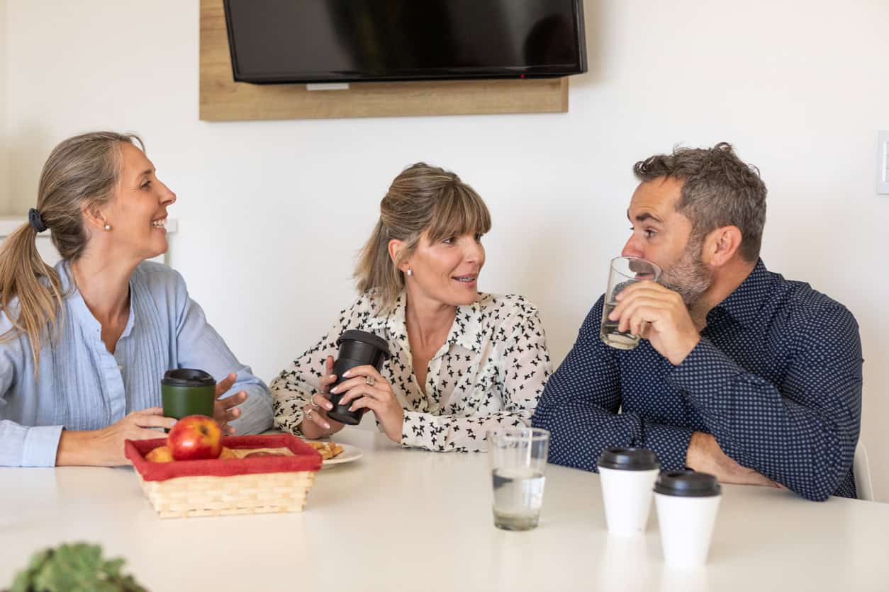 Two women and a man chatting over coffee at a table