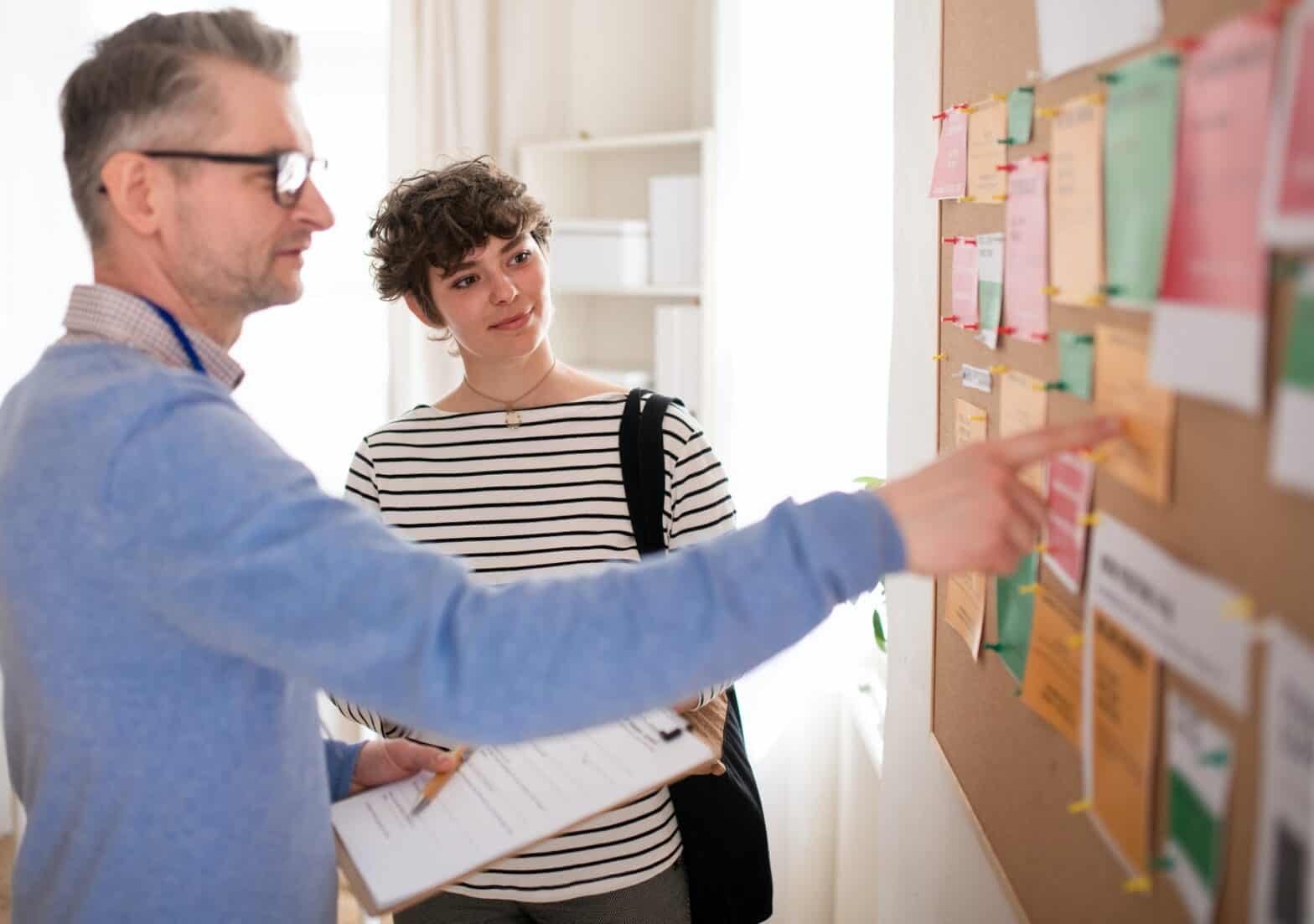 Woman looking at a noticeboard where a man next to her is pointing