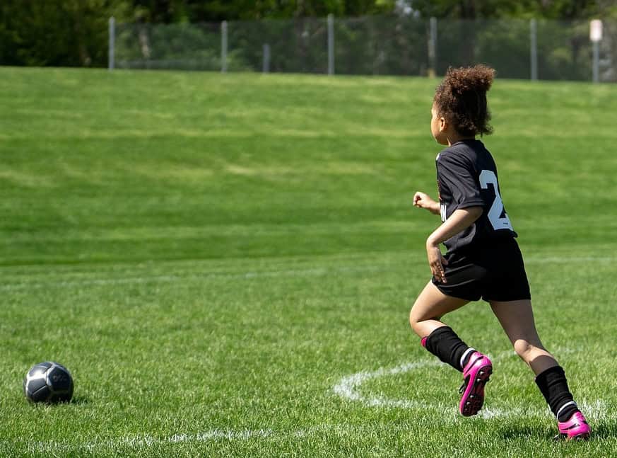 Young girl kicking a football on a pitch