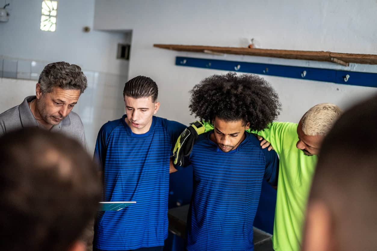Young men huddling in prayer in a football changing room.