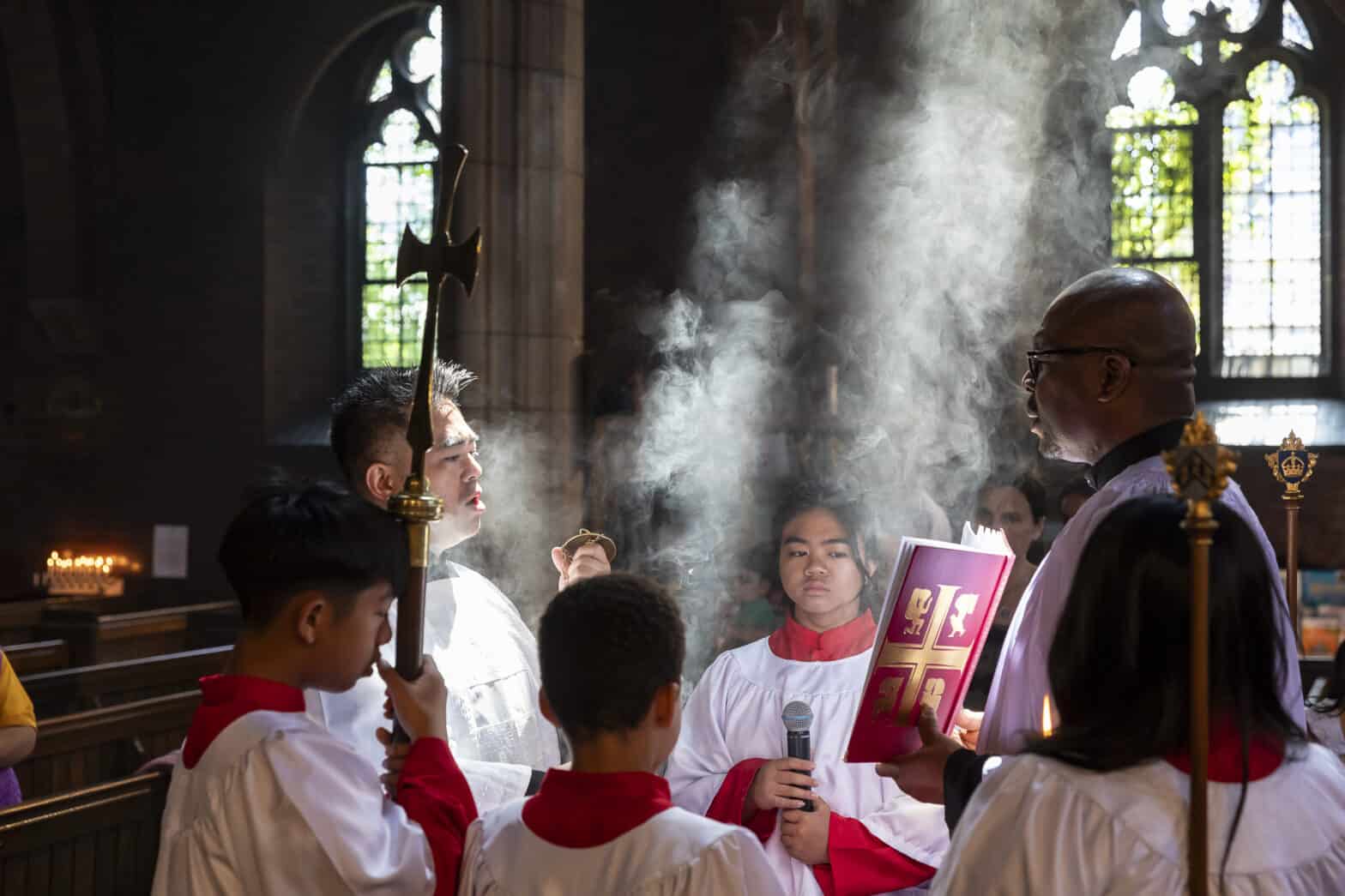 Group of people standing reading a Bible with incense highlighted by the sun's rays