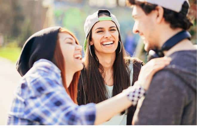 Three young people talking and laughing together. They are wearing casual clothes, including a baseball cap.