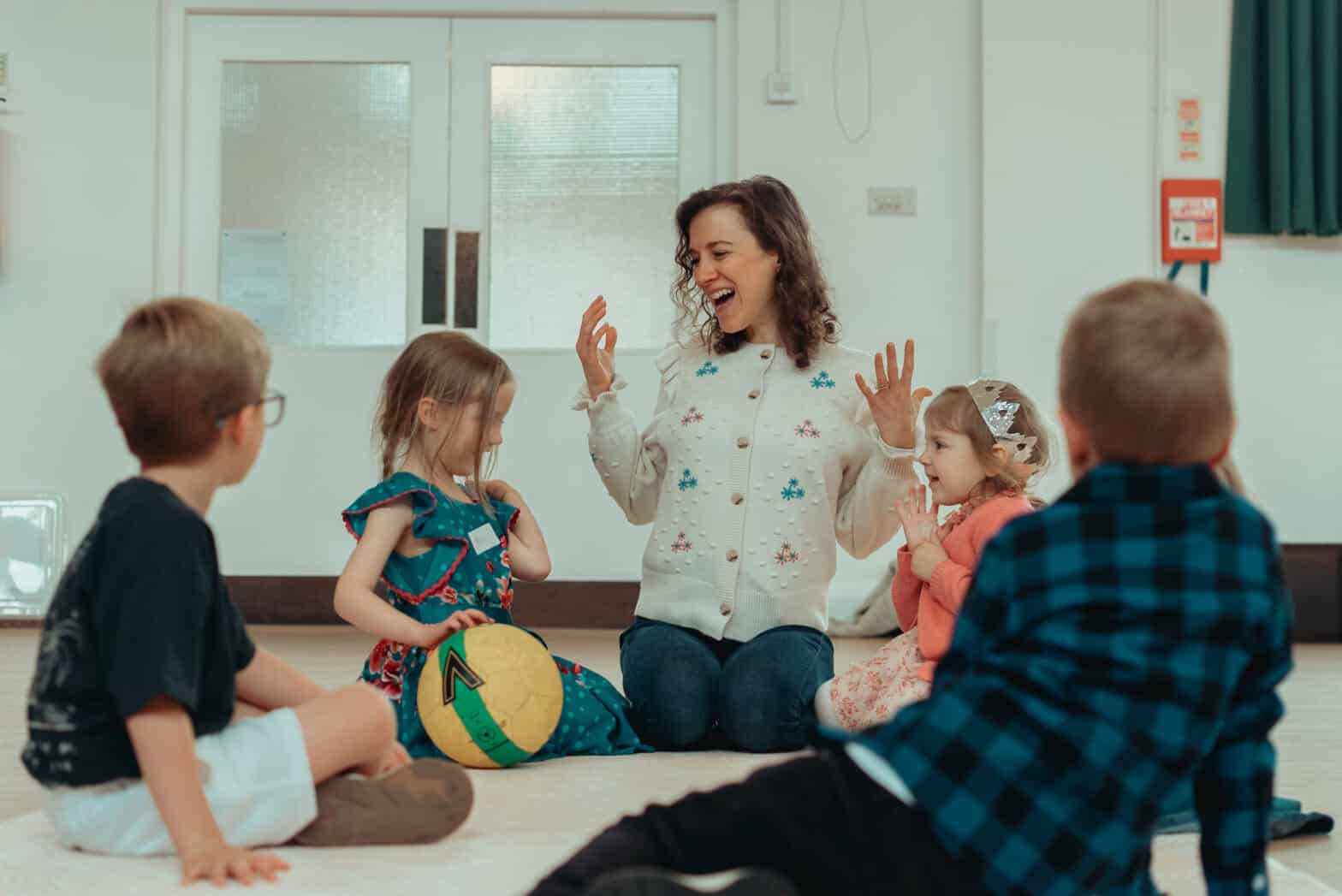 Woman sitting with four children on the floor of a church hall, teaching them in a Sunday school-style setting