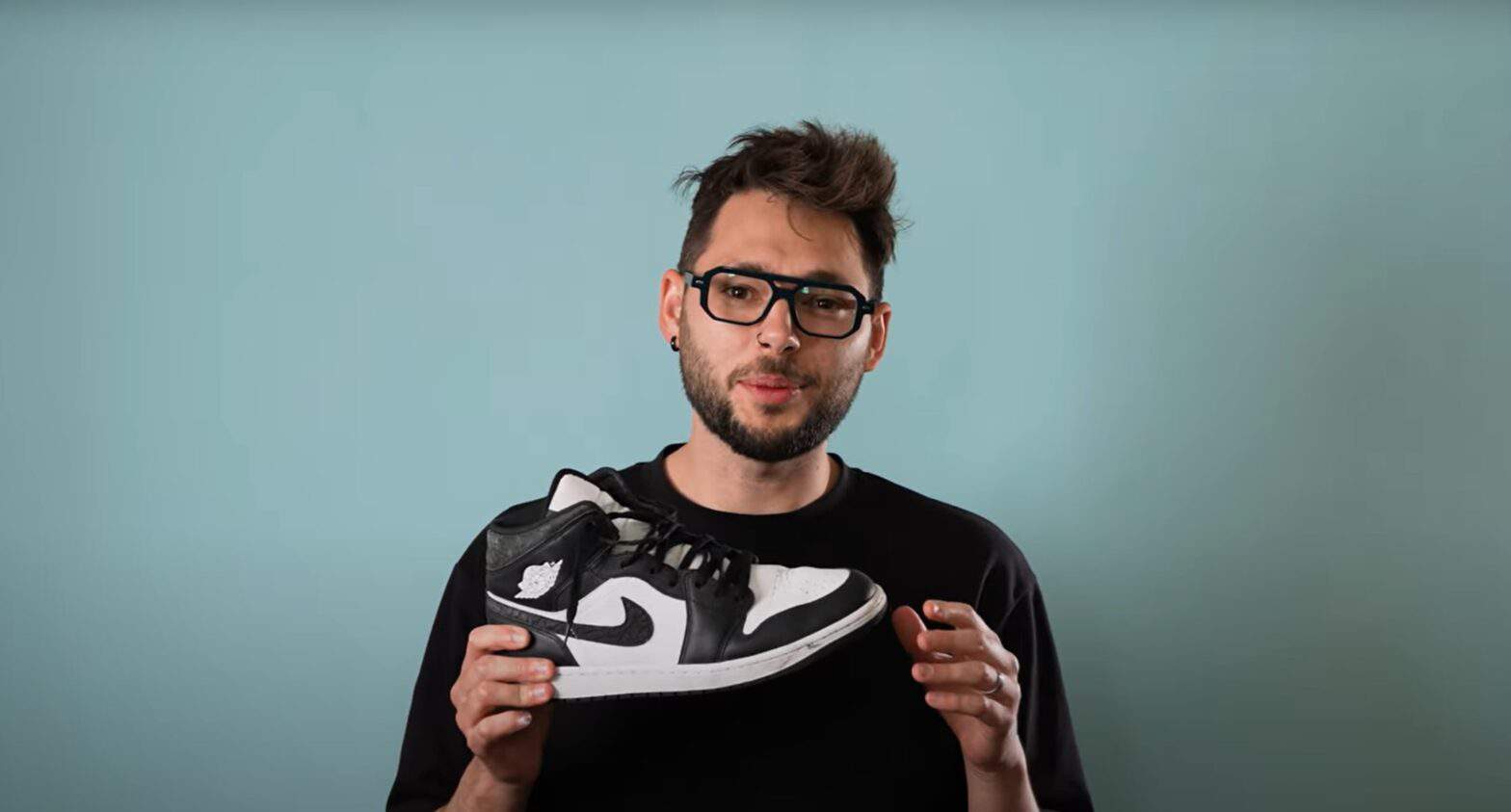 Man holding a black and white tennis shoe and talking about it