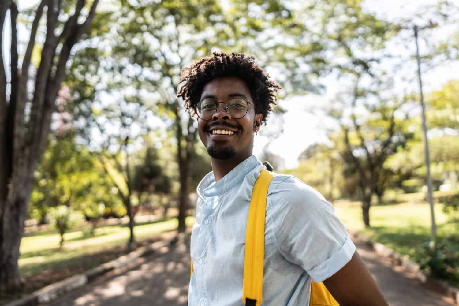Young gentleman of colour with short sleeve shirt and bright yellow back pack smiling in the outdoors