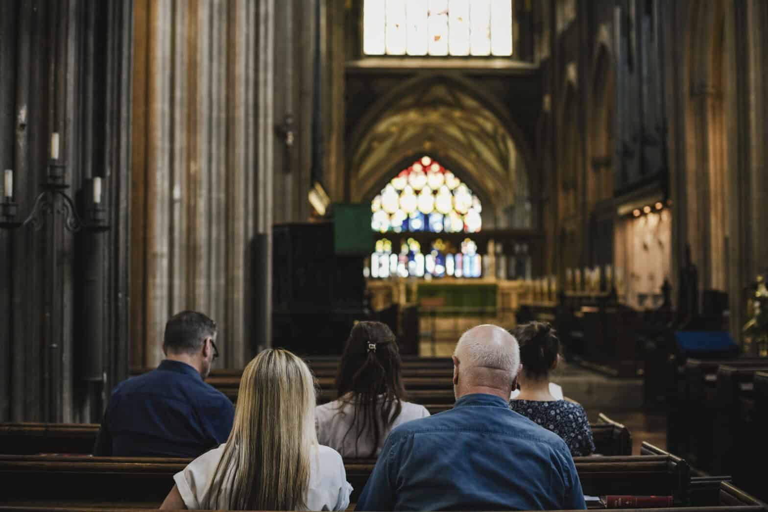 People siting in the pews of a large traditional church with pillars, stained glass and an altar