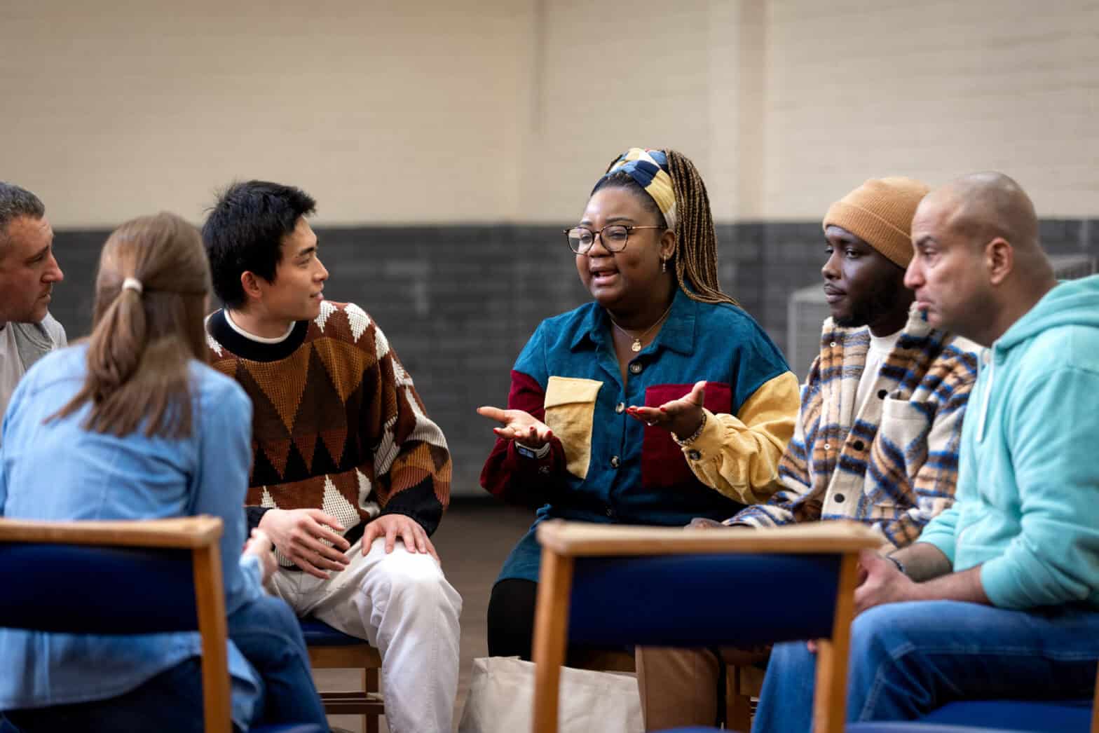 A group of adults sitting in a circle and talking to each other in a community centre.