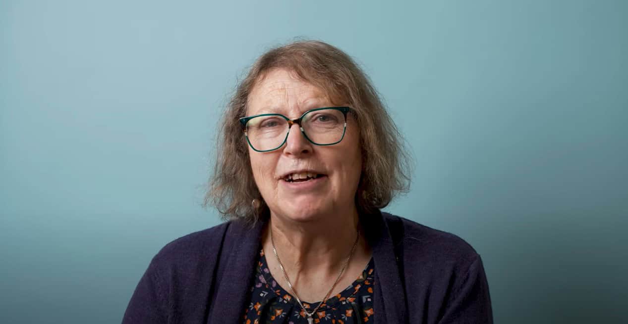 Woman wearing glasses is speaking against a blue background