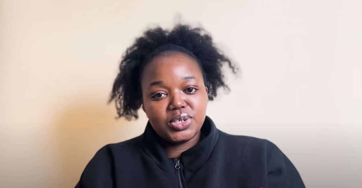 Woman in black top speaking against beige background