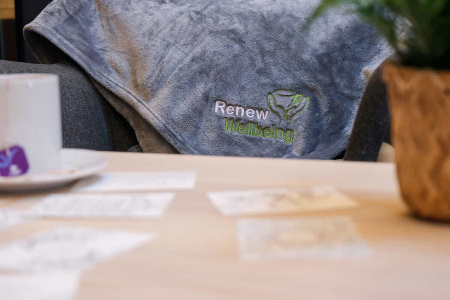 Blanket and cup of tea with 'Renew Wellbeing' embroidered on the blanket