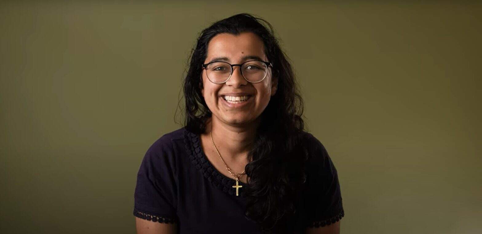 Smiling woman against an olive background wearing a cross