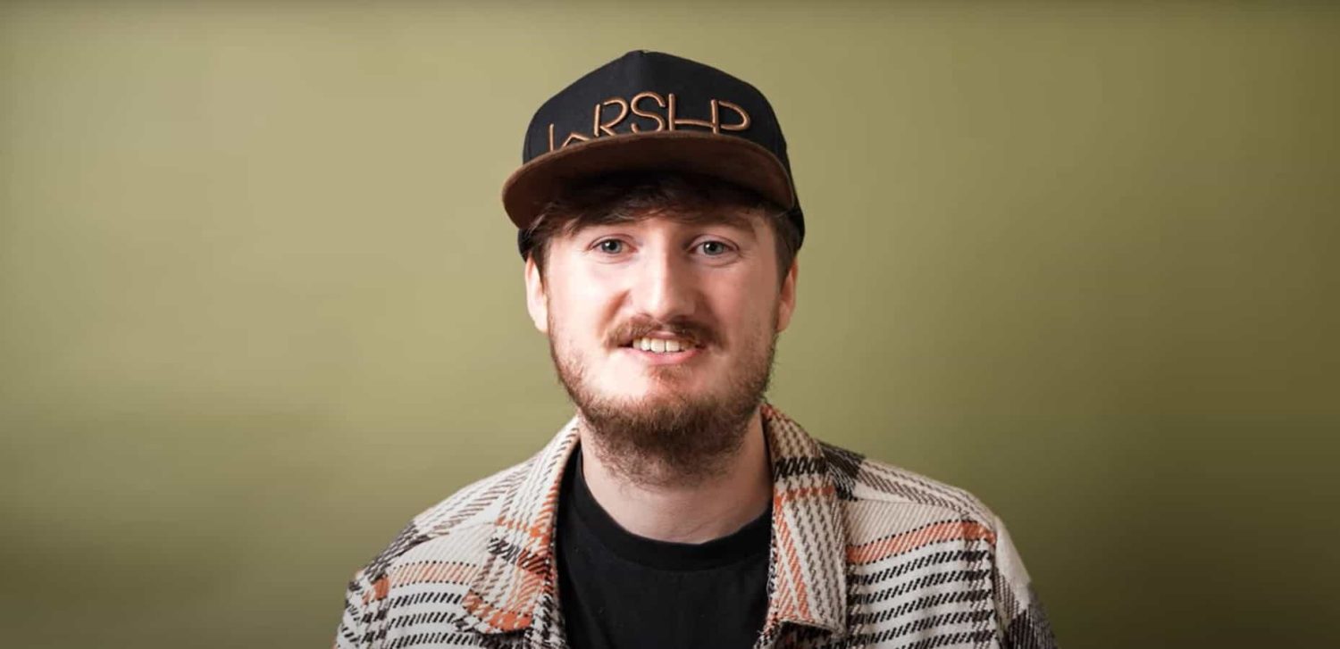 Man wearing a hat with 'WRSHP' ('worship' without vowels) against an olive background