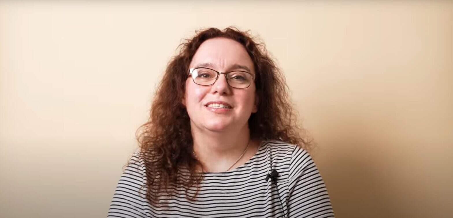 Woman with glasses sharing her story against a beige background
