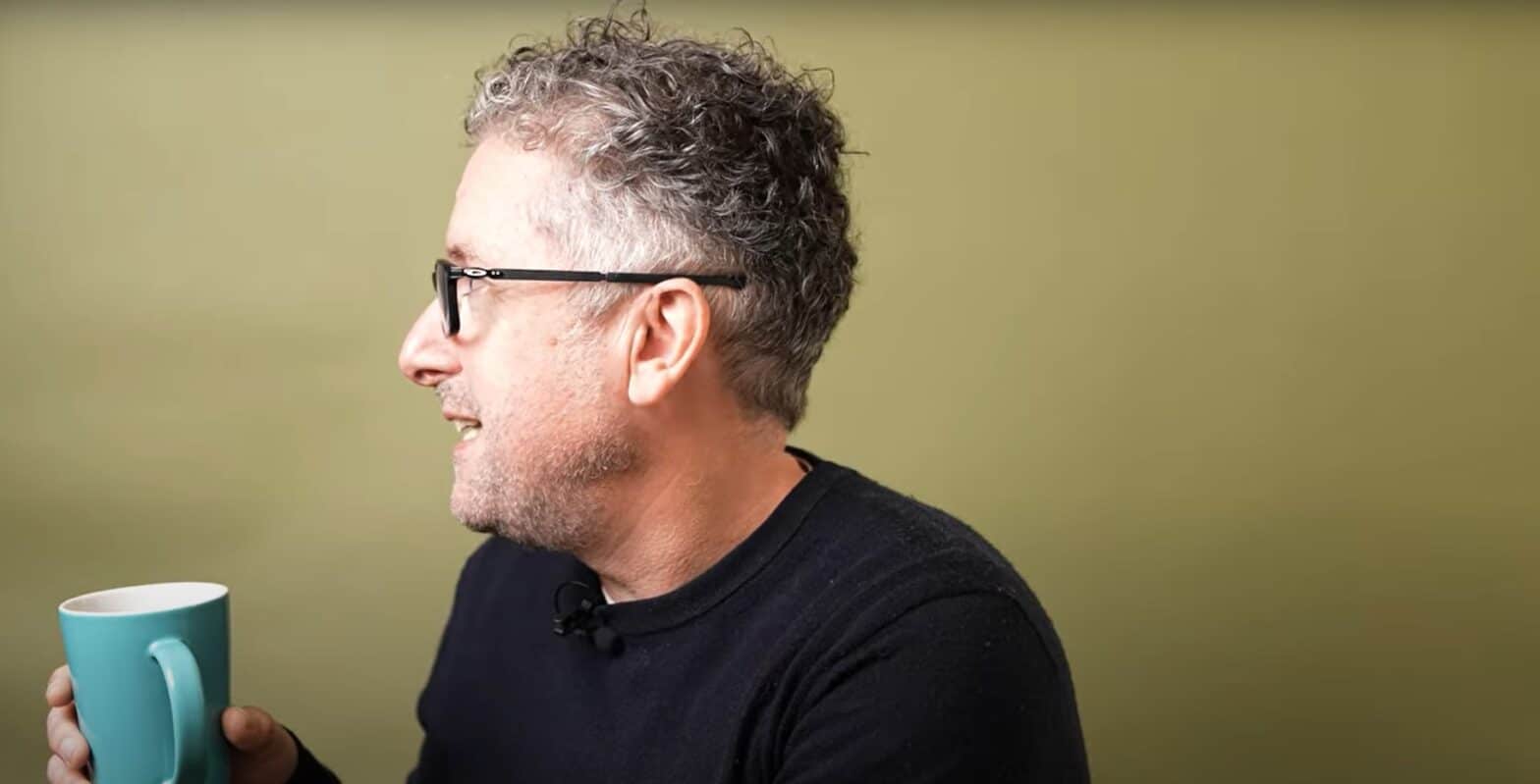 Profile of a man holding a blue coffee mug and talking to someone off the screen