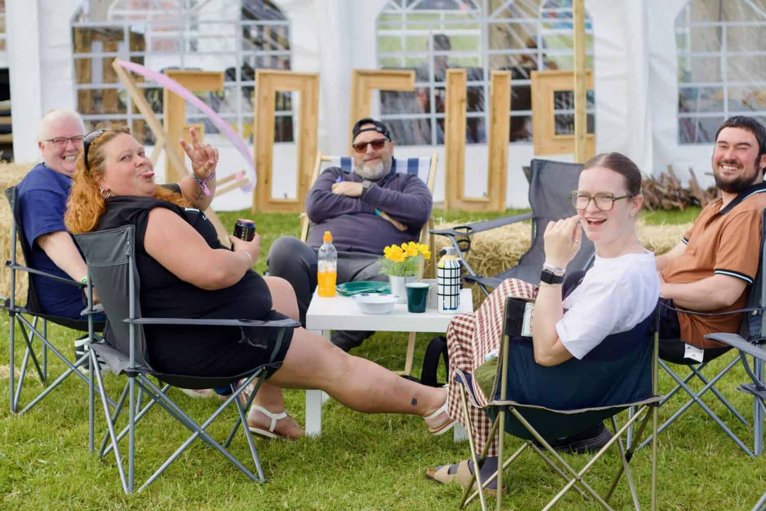 A group of people are sitting outside on camping chairs outside a marquee at a church event. They are smiling and enjoying themselves.