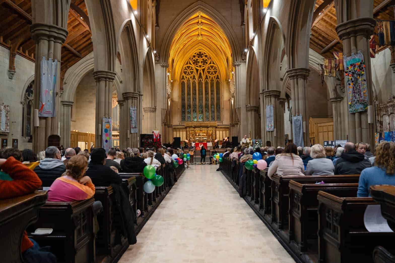 Members of the congegration sitting in pews facing forward where there is a performance taking place inside the church