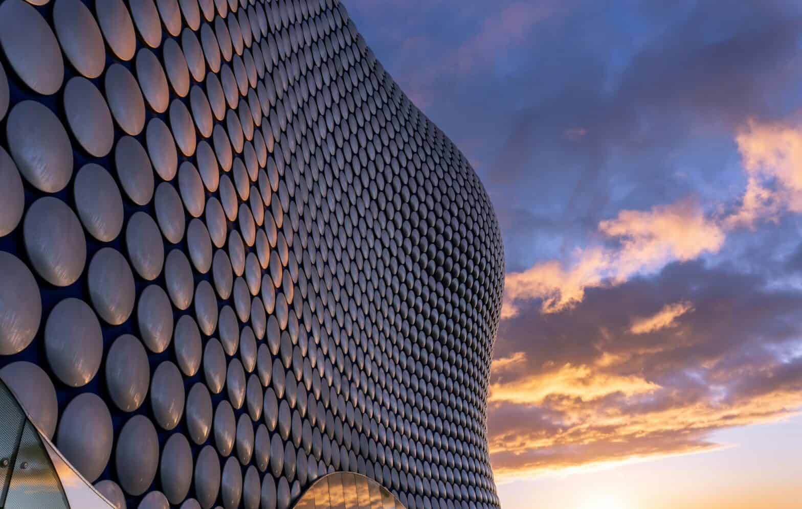 A modern building with metal circular discs against a moody sky with orange and black clouds