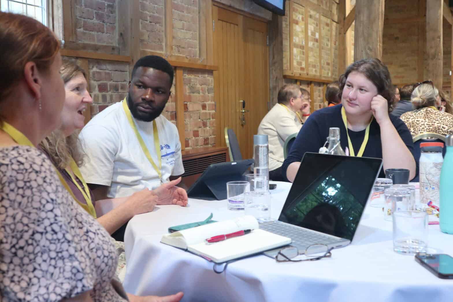 A group of diverse people sitting at a table with laptops and pads in discussion