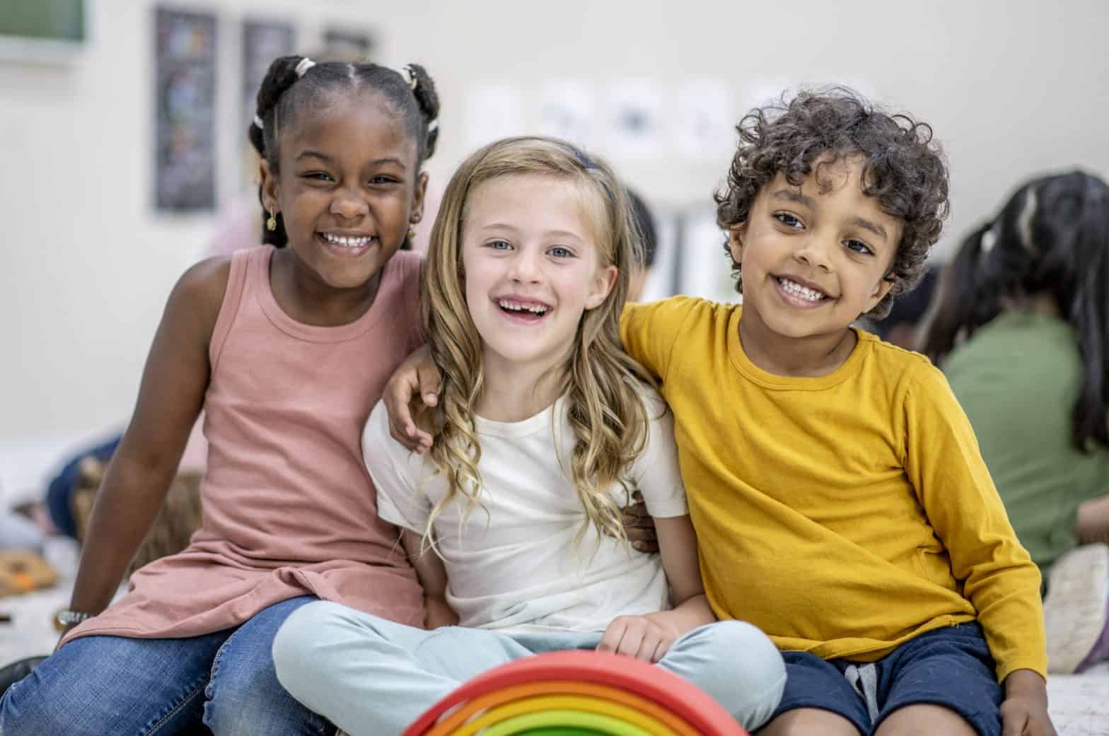 A small group of three school aged children huddle together on an area rug in their classroom