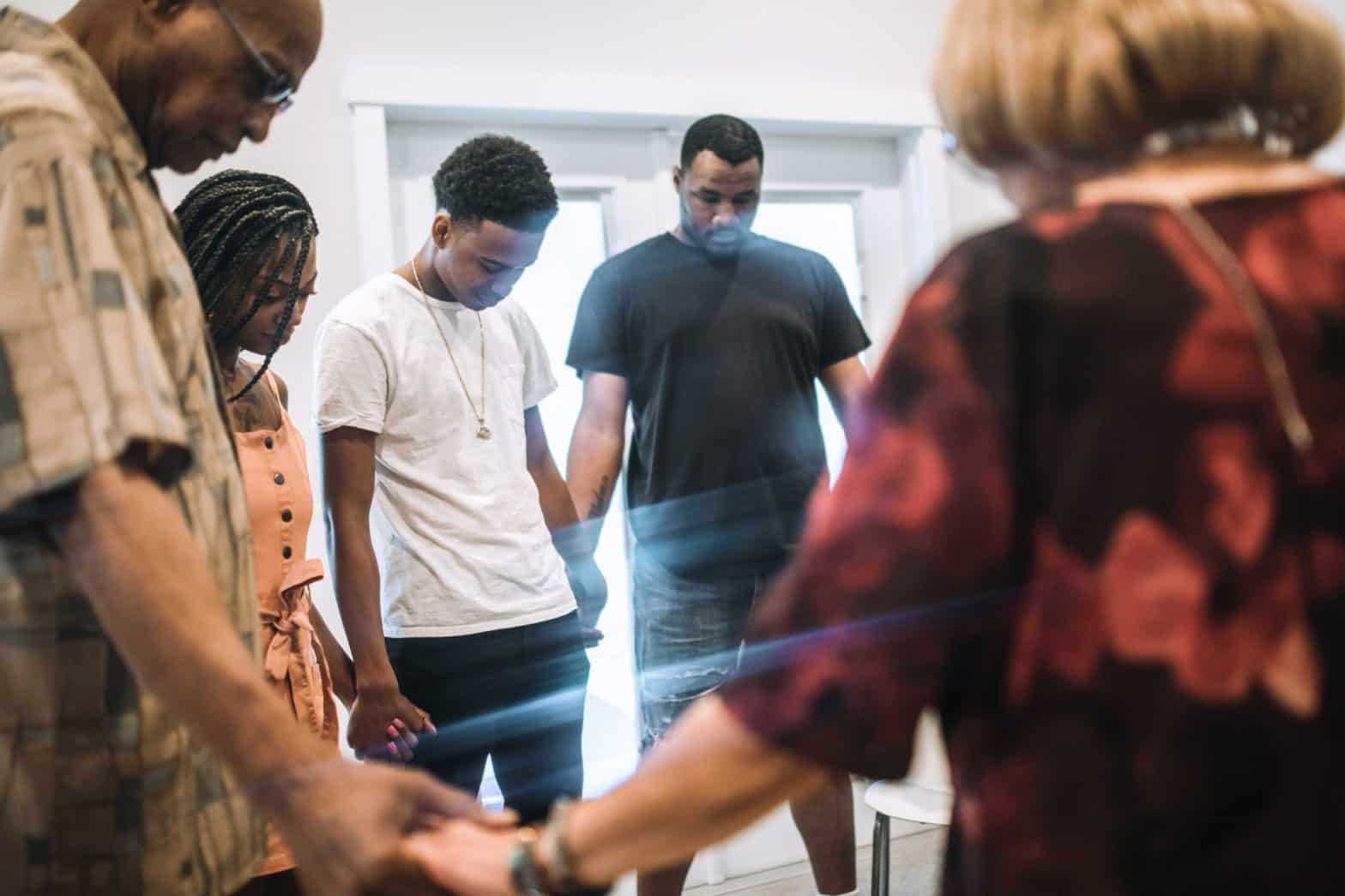 A group of people in a circle holding hands with their heads down praying together
