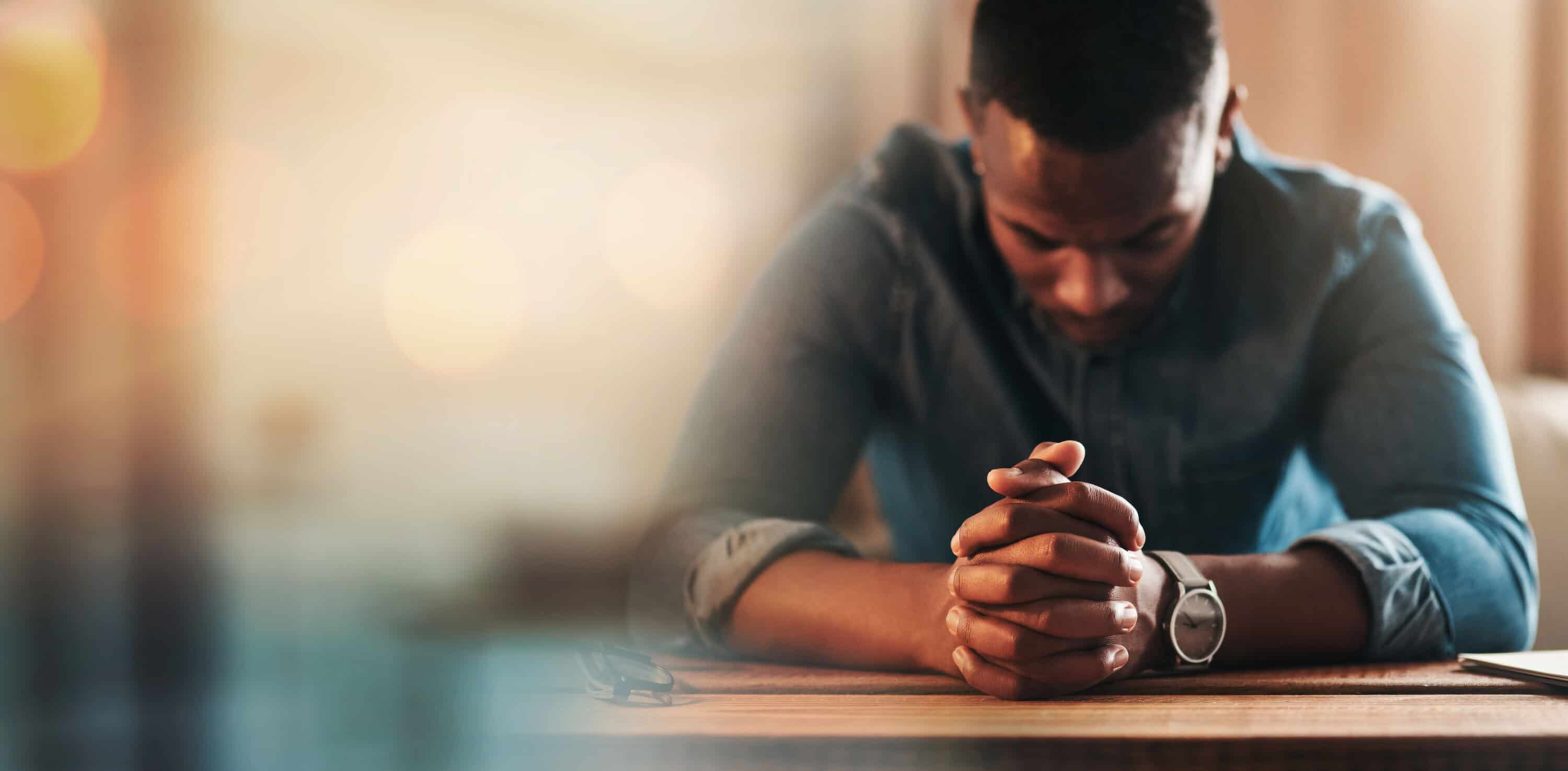A man wearing a blue shirt with his hands in prayer