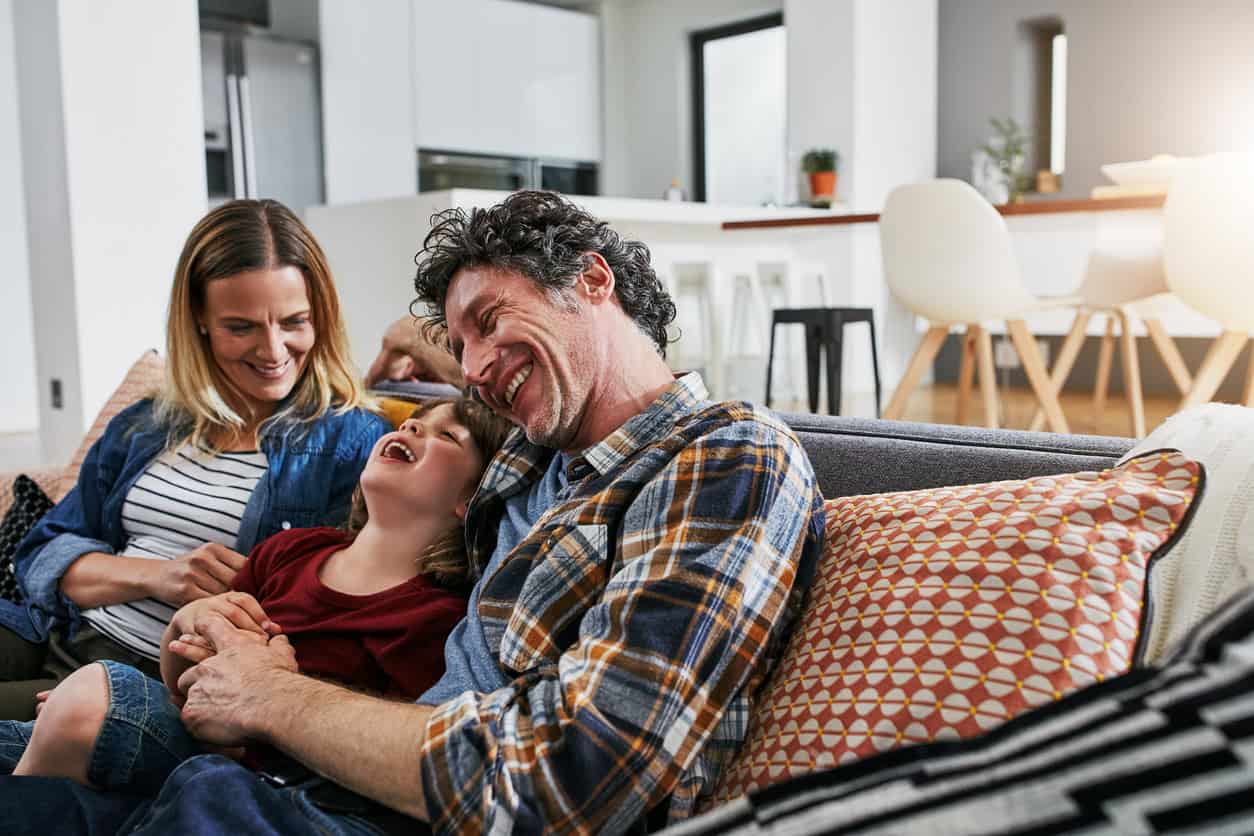 A child laughing sitting in between his parents on the sofa in their house
