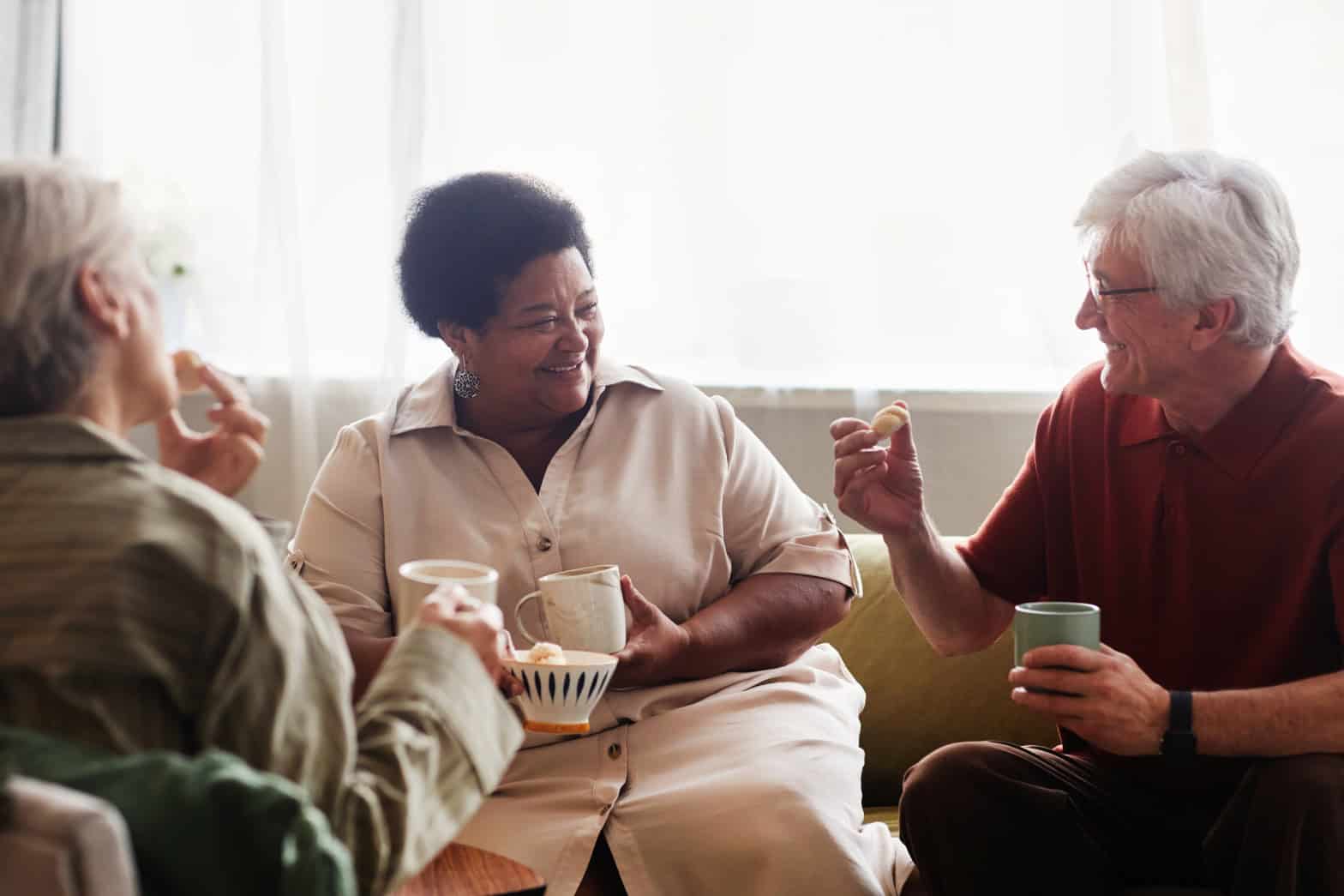 Three older people sitting together drinking tea