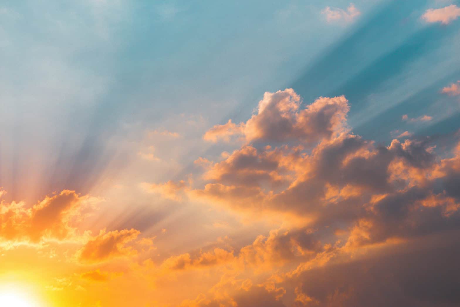 Yellow and orange sunshine bottom left of the picture in a blue sky with shadowy clouds