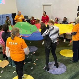 A group of diverse adults and children holding a colourful parachute in a group setting