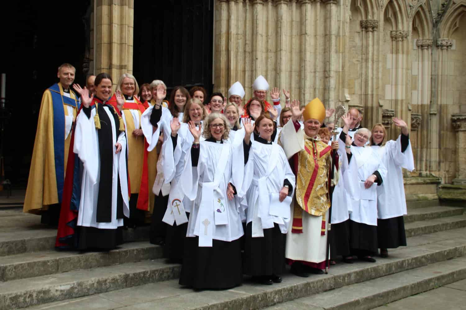 The Archbishop of York standing several ordinands who are waving and smiling to the camera