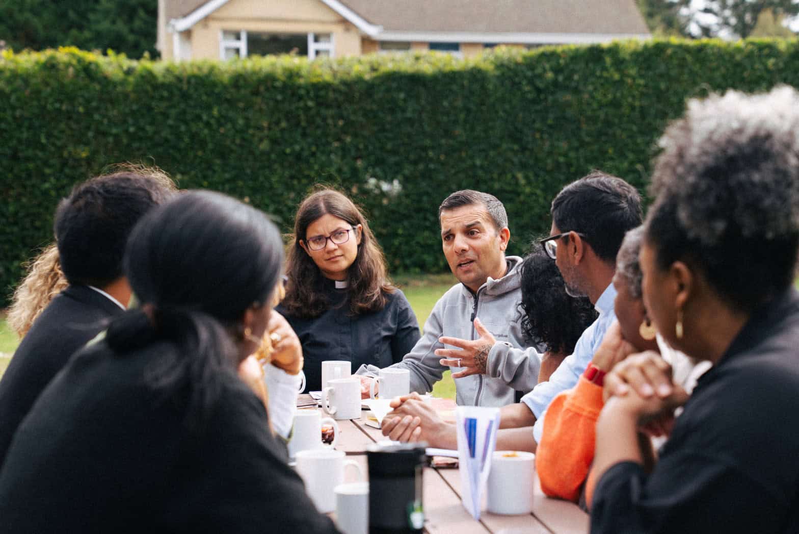 A group of people sitting around a picnic bench all focussed on a gentleman who is explaning something to them.