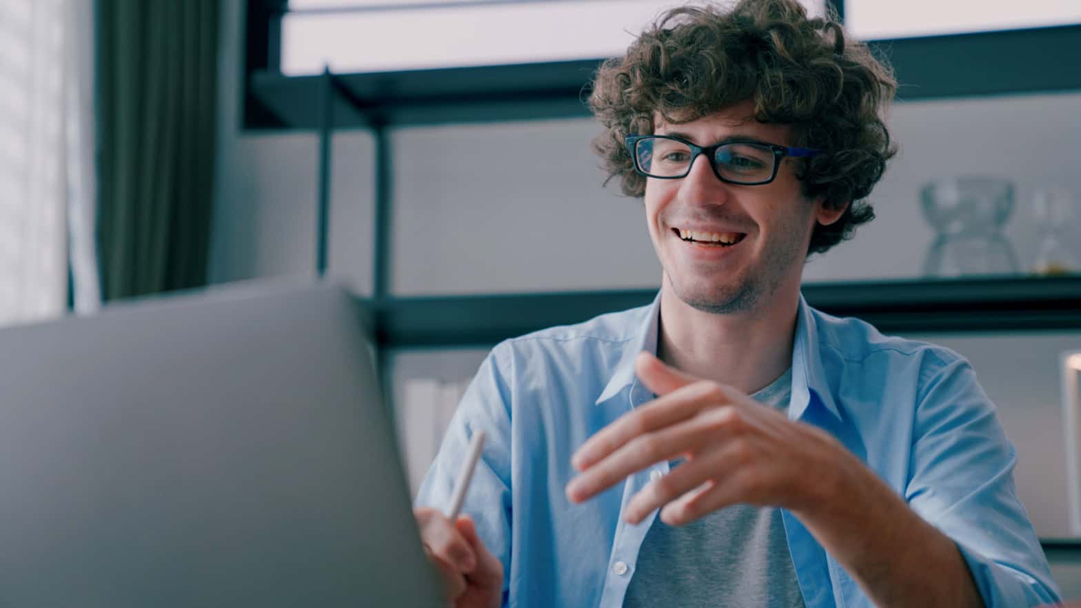 Man with glasses on smiling and gesticulating in front of a laptop